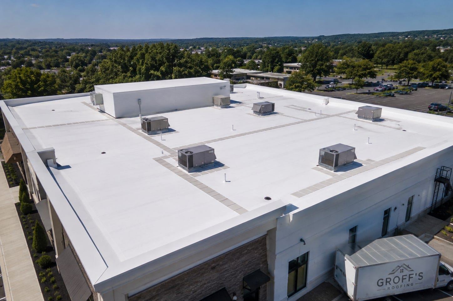 Drone view of a white TPO roof with equipment curbs and a Groff's truck below